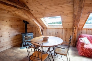 Eine Holzhütte mit einem runden Tisch, Stühlen, einem roten Bett und einem Holzofen.