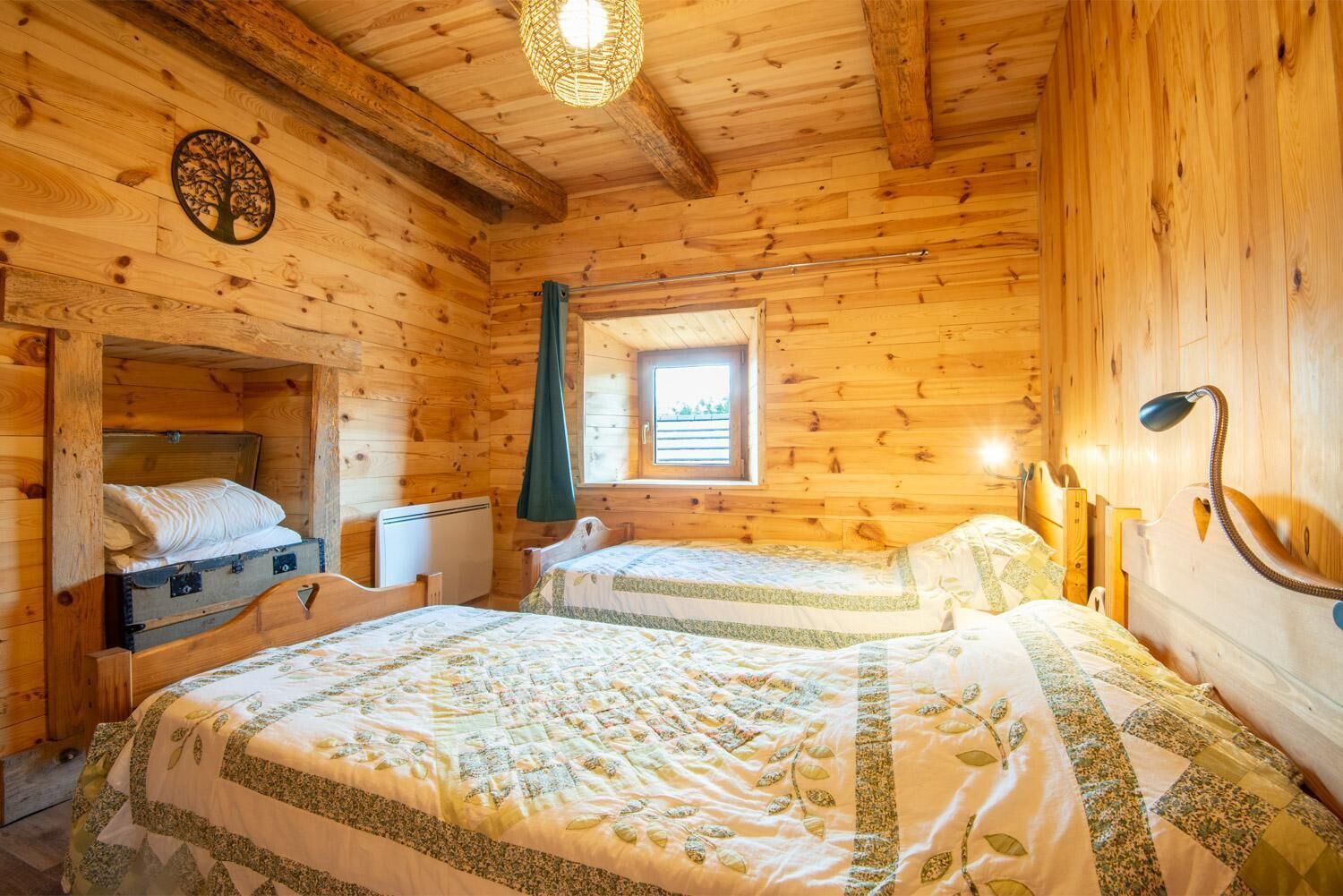 Una habitación de cabaña de madera con dos camas, una ventana, una lámpara en el techo y un calentador fijado a la pared.