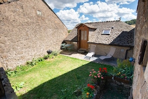 Ein Steinhaus mit einer Holztür, einer kleinen Terrasse mit Grill und einem Blumenbeete