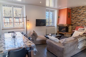 A living room with a fireplace, a dining table, and a sofa. - Gîte de Marthe - PEYRE EN AUBRAC (PEYRE EN AUBRAC)