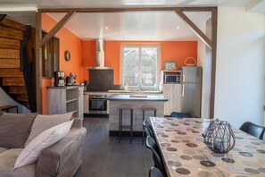 A modern kitchen with a central island, a dining area with a patterned table, and a staircase leading to another level. - Gîte de Marthe - PEYRE EN AUBRAC (PEYRE EN AUBRAC)