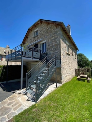 A stone building with a balcony and a staircase leading to an upper level. - Gîte de Marthe - PEYRE EN AUBRAC (PEYRE EN AUBRAC)