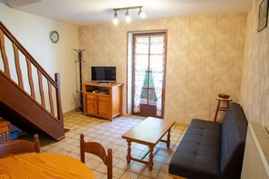 Ein Wohnzimmer mit einer Holztreppe, einem Fernseher auf einer Holzkommode, einem Sofa, einem Esstisch und einem Sessel.