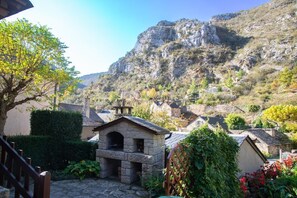 Ein Steinhaus mit einer kleinen Veranda, umgeben von Grünpflanzen und einer Bergkulisse.