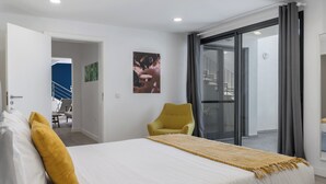 Una camera da letto con un letto, una poltrona gialla, un'ampia finestra e un portone che dà su un balcone.