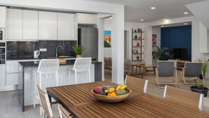 Una cucina moderna con mobili bianchi, un frigorifero in acciaio inossidabile e un'area pranzo con tavolo in legno e sedie bianche.