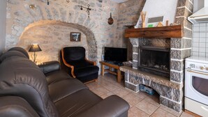 A living room with a stone wall, a fireplace, a television, and a sofa. - Gîte Betty in Laval du Tarn (LAVAL DU TARN)