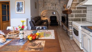 A cozy living room with a fireplace, a dining area with a table set for a meal, and a kitchen with a stove and oven. - Gîte Betty in Laval du Tarn (LAVAL DU TARN)