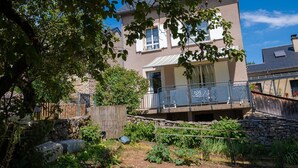 A two-story house with a balcony, surrounded by a garden with various plants and a wooden fence. - Gîte Betty in Laval du Tarn (LAVAL DU TARN)