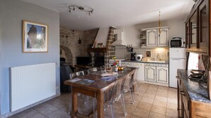 A kitchen with a stone wall, a dining table with chairs, a microwave, and cabinets. - Gîte Betty in Laval du Tarn (LAVAL DU TARN)
