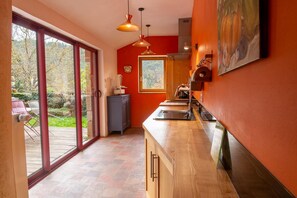 A kitchen with a large sliding glass door leading to a patio, a wooden countertop, and a red wall. - Chez MamieThé - ISPAGNAC (ISPAGNAC)