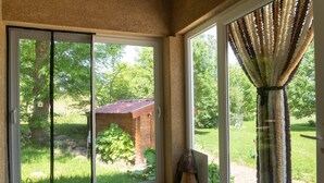 Une pièce dotée d’une porte-fenêtre coulissante donnant sur un jardin, d’une structure en bois et d’un rideau.