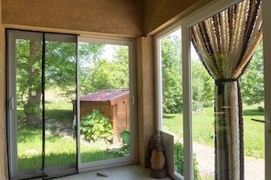 A room with a sliding glass door leading to a garden, a wooden structure, and a curtain. - La Source du Cellier 4/6 persons (SAINT-JEAN-LA-FOUILLOUSE)