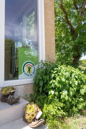A window with a poster of 'Gîte Lozère' and a green bush beside a building. - La Source du Cellier 4/6 persons (SAINT-JEAN-LA-FOUILLOUSE)
