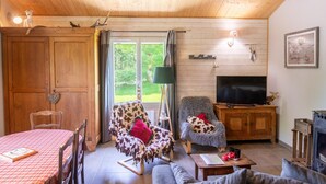 Un salon chaleureux avec un plafond en bois, une télévision, une cheminée et un coin repas comprenant une table et des chaises.