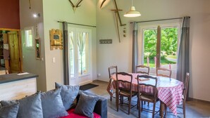 Une pièce comprenant une table à manger dressée pour quatre personnes, un canapé avec des coussins, une grande fenêtre avec des rideaux et un crâne de cerf accroché au mur.