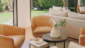 Un salon moderne avec des canapés en cuir, une table basse et une vue sur un panier de basketball et la verdure à l’extérieur.