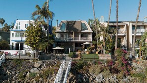 A multi-story residential building with a balcony, surrounded by tropical vegetation and a rocky landscape.