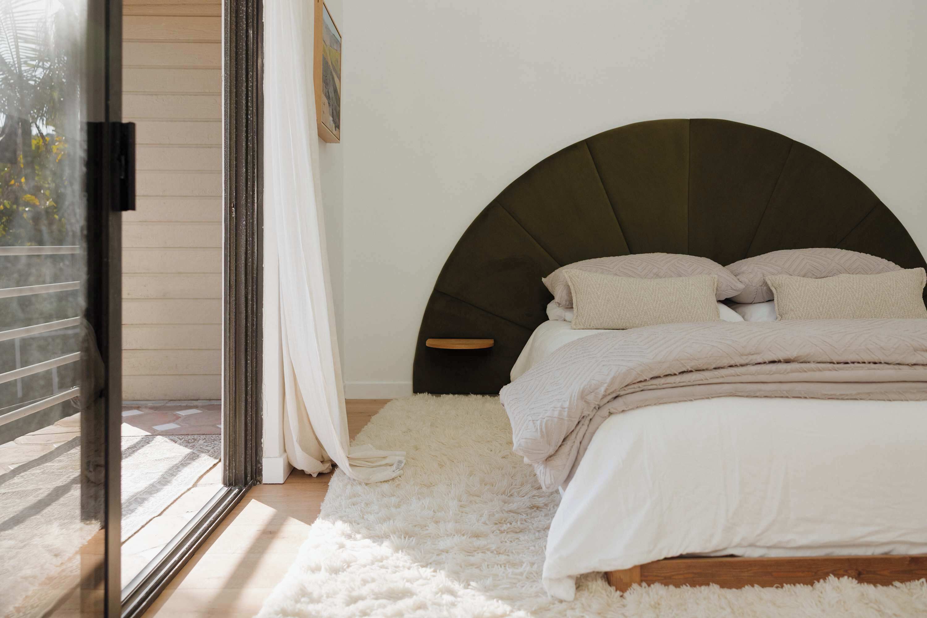A bedroom with a bed, a large window, and a white rug.