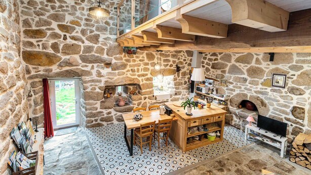 Una stanza con pareti in pietra, un tavolo da pranzo in legno, sedie, un camino e una televisione.