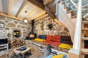 A stone-walled room with a fireplace, a wooden staircase, and a cushioned seating area. - Gîte Castel Cailloux - LE PONT-DE-MONTVERT (LE PONT-DE-MONTVERT)