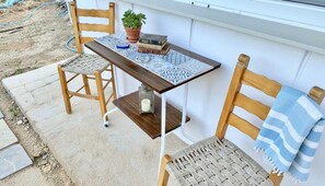 Eine Terrasse mit einem Holztisch, zwei Stühlen, einem Blumentopf und einem Stapel Bücher.