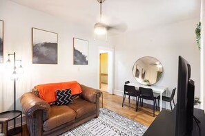 A living room with a brown leather sofa, a round mirror, a dining table with chairs, and framed artwork on the walls. - City Oasis: Walk to Bars, Shops & SLC Attractions (Salt Lake City)