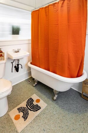 A bathroom with a white bathtub, an orange shower curtain, a white sink, and a toilet. - City Oasis: Walk to Bars, Shops & SLC Attractions (Salt Lake City)