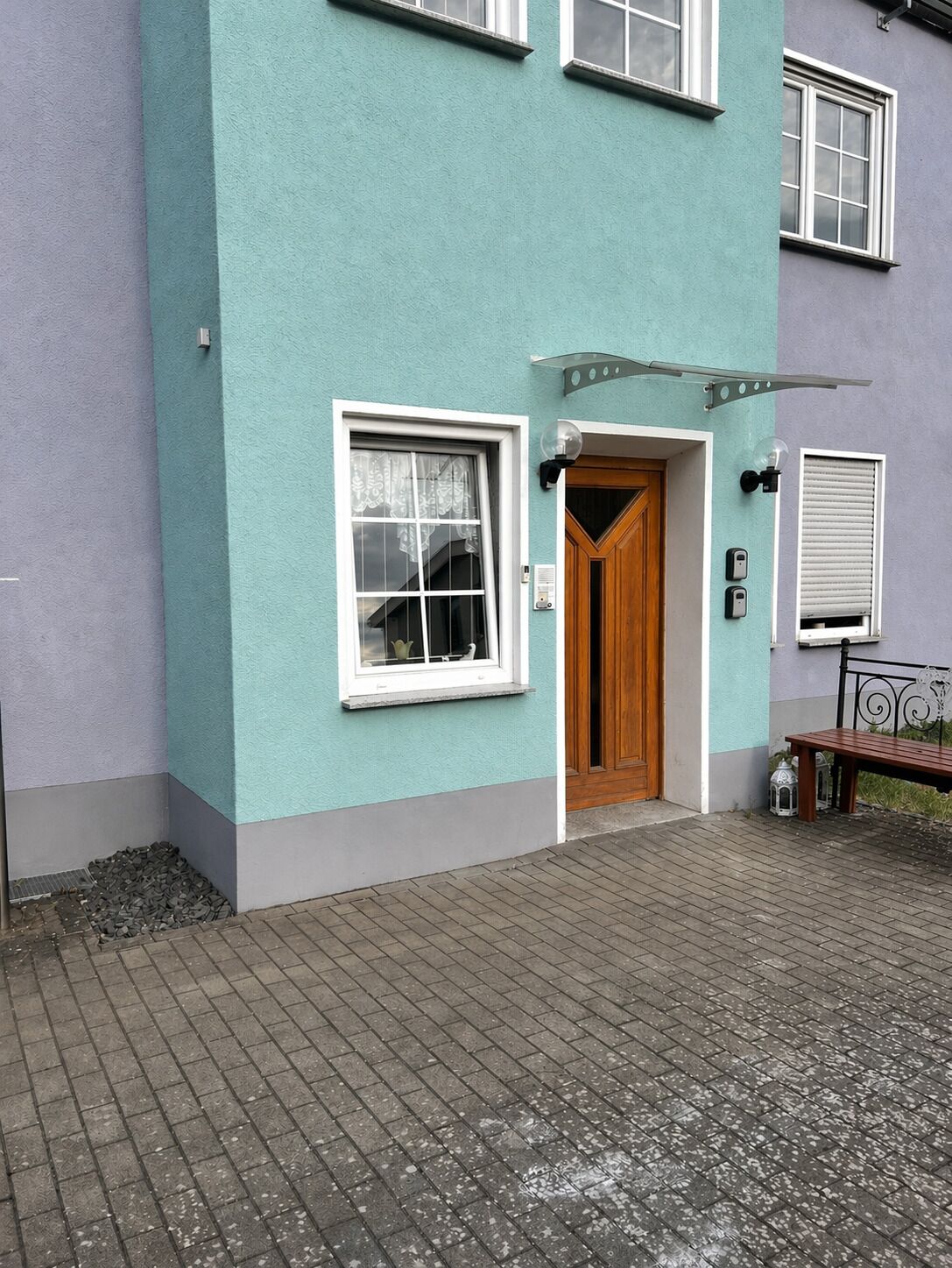 A two-story building with a teal facade, a wooden door, and a small window with a curtain.