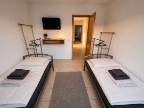 A room with two beds, a TV mounted on the wall, a small shelf with a plant, and a door leading to another room. - Vacation apartment / apartment for fitters / parking lot / WLAN / kitchen / 120QM (Urbar)