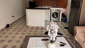 Olohuone, jossa on valkoinen sohvapöytä, ja taustalla näkyy keittiötila sekä jääkaappi.