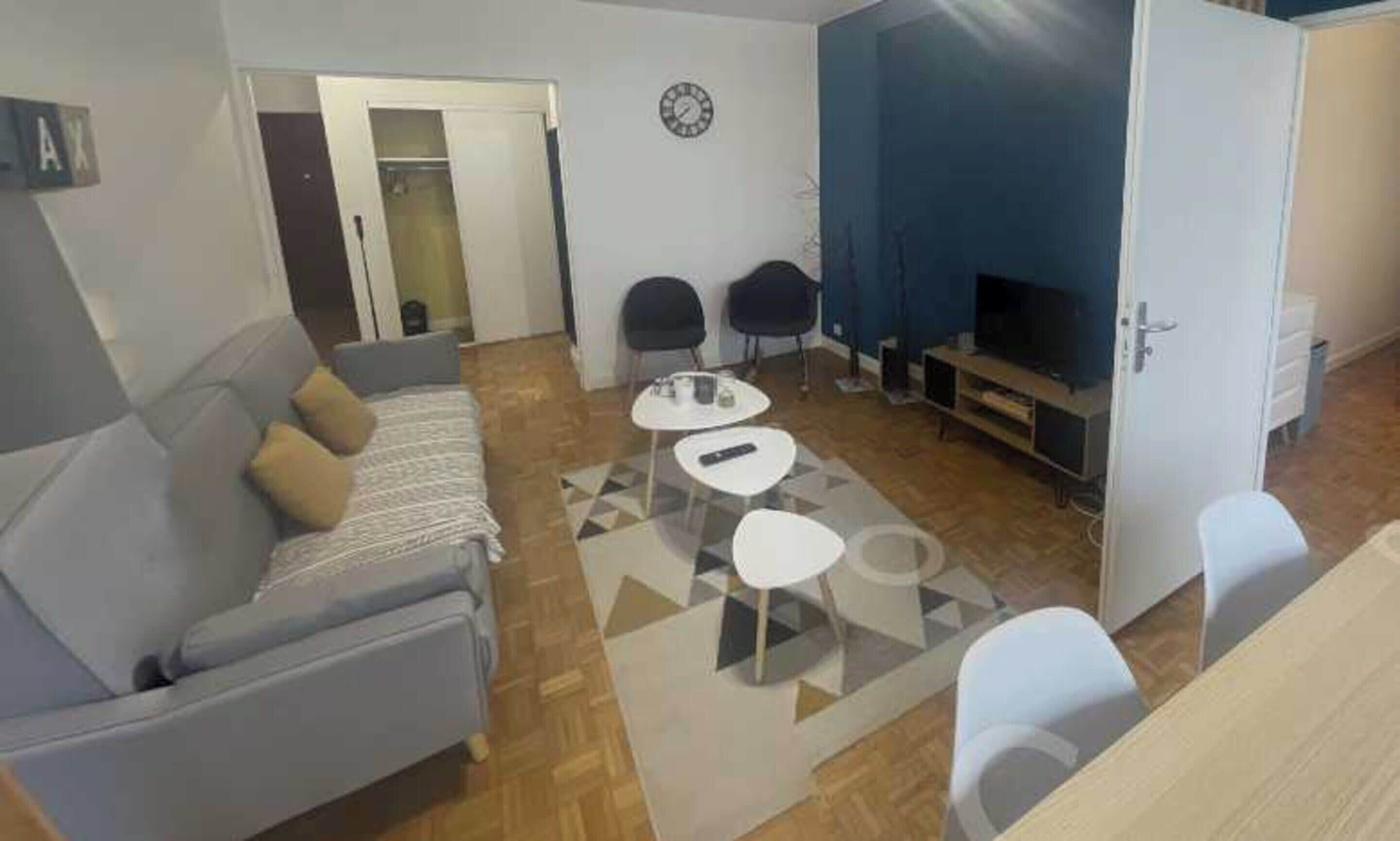 A living room with a sofa, two chairs, a coffee table, a TV, and a clock on the wall.