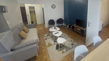 A living room with a sofa, two chairs, a coffee table, a TV, and a clock on the wall.