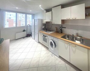 A compact kitchen with a washing machine, a gas stove, and a sink. - Private Room in a Shared Flat - Villeurbanne (Villeurbanne)