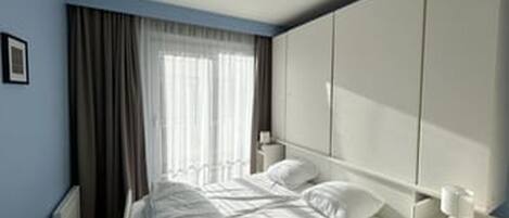 Une chambre à coucher comprenant un lit, une table de chevet, une armoire et une fenêtre avec des rideaux.
