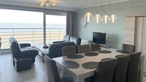 Uma sala de estar moderna com área de jantar, janelas amplas e vista para a praia.