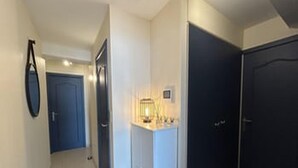 Um corredor com uma porta azul, uma mesa pequena com abajur e uma porta escura.