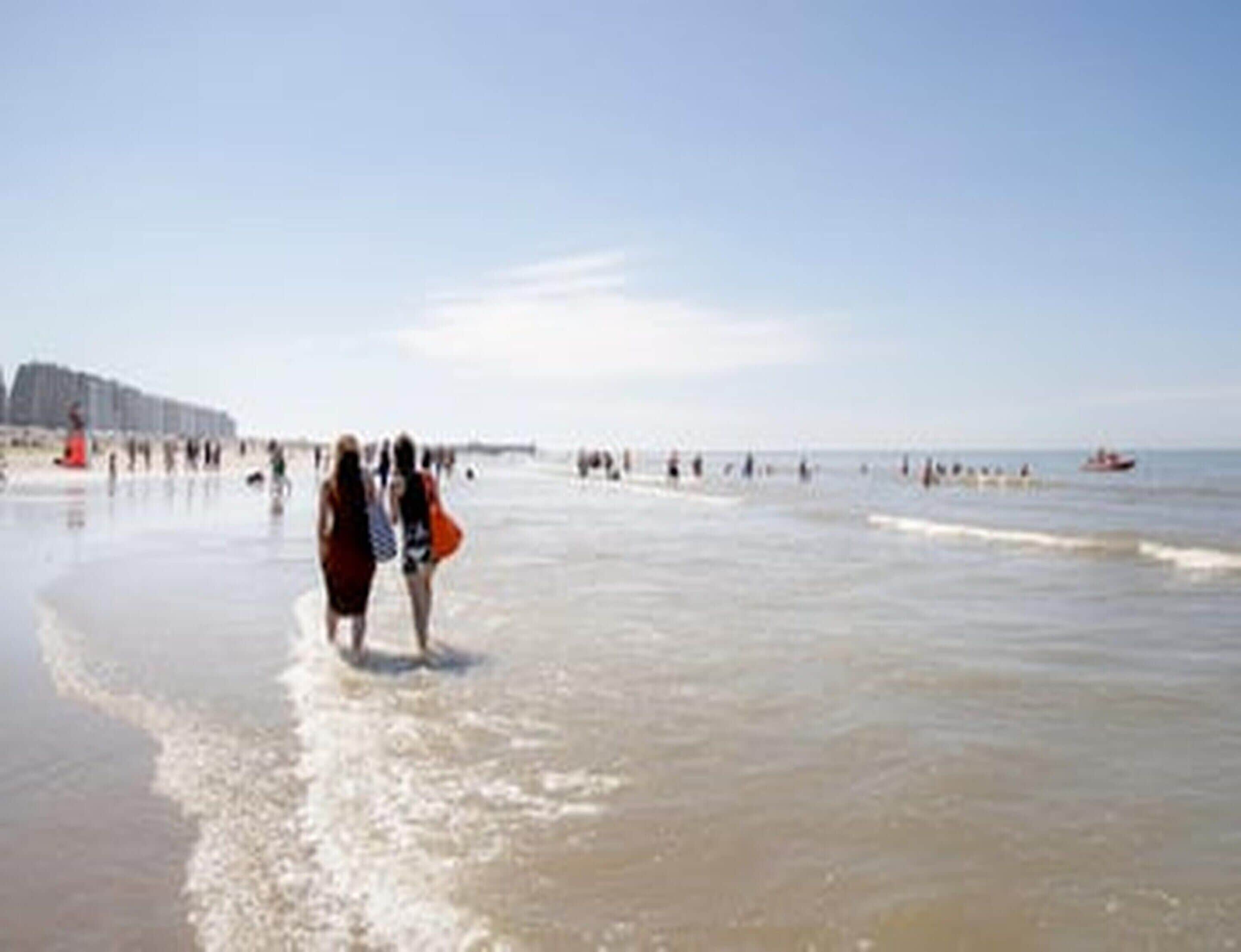 Ein Strand mit Menschen, die am Ufer entlanggehen, und einem Pier im Hintergrund.
