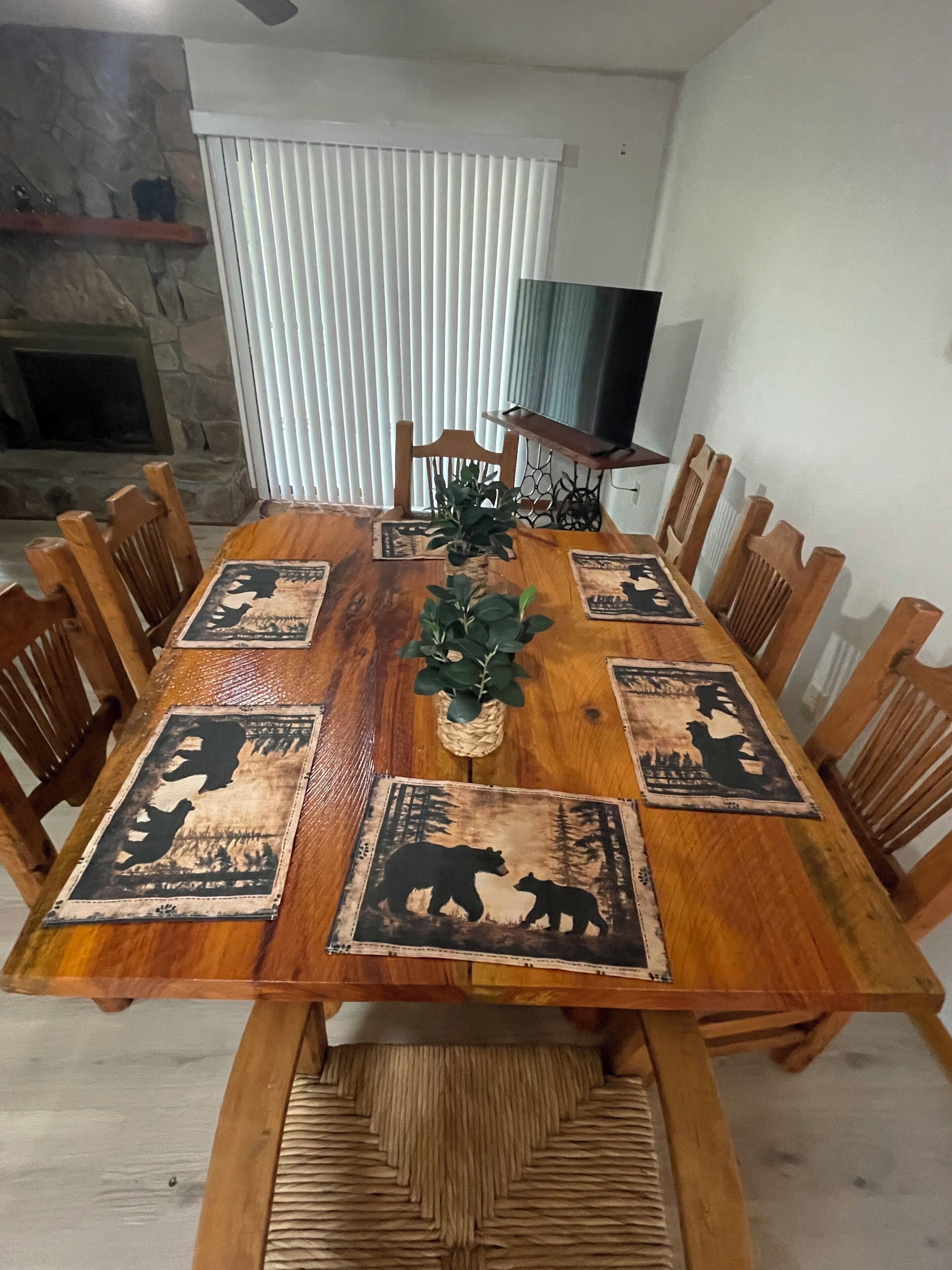 Une table à manger avec des chaises en bois, une plante placée au centre et des sets de table ornés de motifs d’ours.