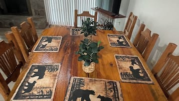 Une table à manger avec des chaises en bois, une plante placée au centre et des sets de table ornés de motifs d’ours.