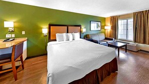 Une chambre d’hôtel comprenant un lit, un bureau, une chaise, un canapé, une fenêtre avec des rideaux et des lampes fixées au mur.