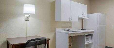 A compact kitchenette with a white countertop, sink, and a small refrigerator.