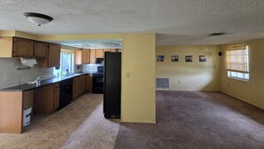 A spacious kitchen with wooden cabinets, a black refrigerator, and a tiled floor. - 2-bedroom house in peaceful Port Richey with cool AC (Port Richey)