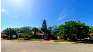 A suburban street with houses, a clear sky, and a parked car. - 2-bedroom house in peaceful Port Richey with cool AC (Port Richey)