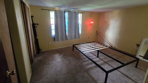 A room with a bed frame, a window with curtains, a door, and a wall-mounted light fixture. - 2-bedroom house in peaceful Port Richey with cool AC (Port Richey)