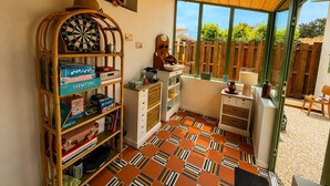 Een kamer met een dartbord, planken met boeken en spelletjes, een raam met uitzicht op een houten schutting, en een kamer met een vloer met patroon.