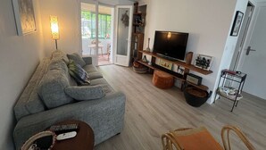 Een woonkamer met een bank, een televisie, een lamp en een schuifdeur naar een buitenruimte.
