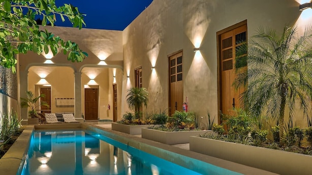 Una piscina con superficie d'acqua cristallina e blu, circondata da un edificio con diverse porte e finestre e una facciata ben illuminata.