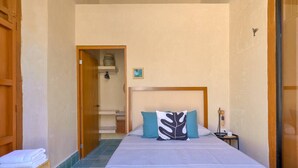 Een slaapkamer met een bed, kussens, een nachtkastje, een lamp en een houten deur.