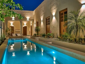 Una piscina con superficie d'acqua cristallina e blu, circondata da un edificio con diverse porte e finestre e una facciata ben illuminata.